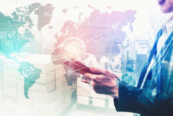 Hand holding a tablet in front of a world map of supply routes
